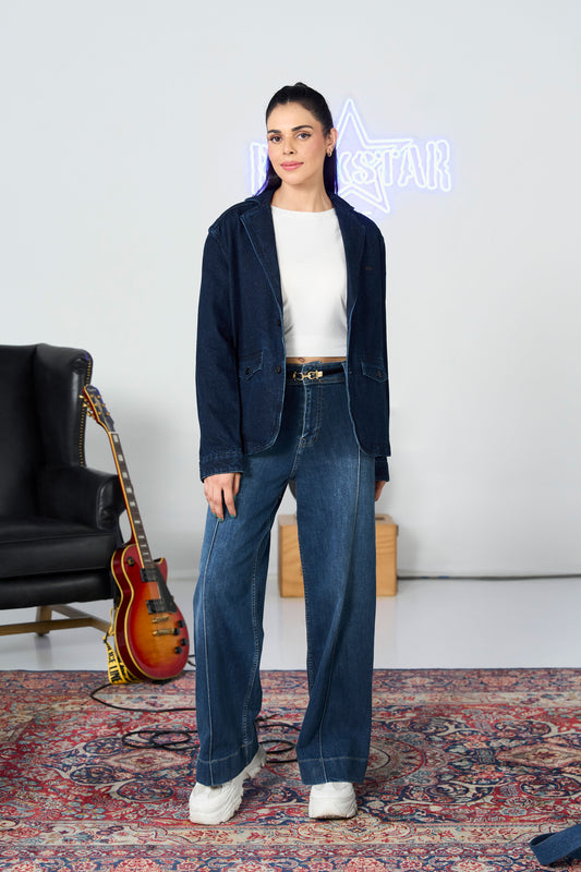 Woman in a navy blazer and blue jeans standing in a room with a guitar and neon sign.
